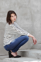 Natural light outdoors portrait of young fashionable brunette woman practicing model posing outdoors against urban style background of grey concrete wall stairway