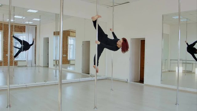 Young pole dance woman in black clothes can not hold herself in pose on pylon