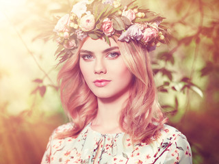 Beautiful blonde woman with flower wreath on her head. Beauty girl with flowers hairstyle. Girl in a summer forest. Fashion photo