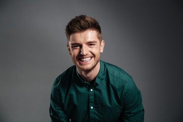 Happy young man sitting isolated over grey background