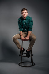 Fototapeta na wymiar Smiling young man sitting isolated over grey background