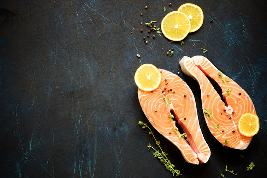 Steak raw salmon with lemon, thyme and pepper on a dark background. View from above