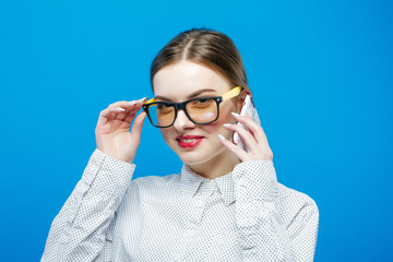 Portrait of Cute Brunette Holding Her Eyeglasses in Hands and Looking at the Camera on Blue Background in Studio.