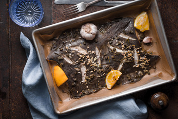 Baking tray with flounder and seasoning on the stone background top view