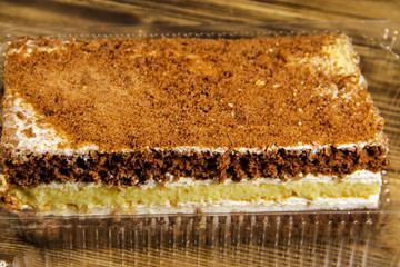 Sour cream cake in plastic container on  wooden table