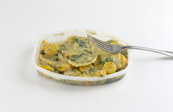 Ravioli with spinach TV dinner with a fork on the tray atop a white tablecloth.