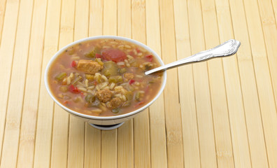 Gumbo with sausage and chicken meat in a small bowl with a spoon in the food on a wood slat place mat.