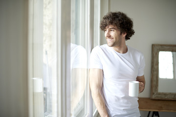 Relaxed young man portrait. Shot of a young man holding a cup of coffee and relaxing while standing by the window. 