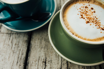 Coffee cappuccino in a green cup on a saucer. Two cups coffee on a wooden table