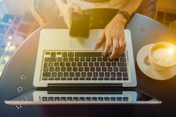 Young woman sitting at desk and typing on laptop and mobile phone ,hands close up. Female working on an outdoor cafe.