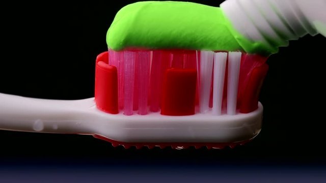 Tooth paste and brush. Applying green toothpaste on red toothbrush against black background .