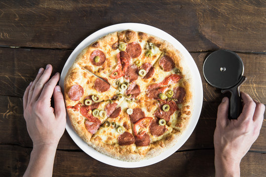 Cropped Shot Of Person Holding Pizza Cutter And Tasty Fresh Pizza On White Plate