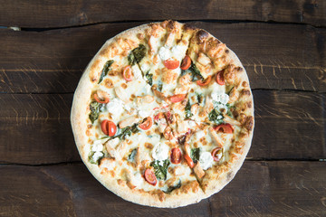 top view of delicious homemade italian pizza with cheese and tomatoes on wooden tabletop