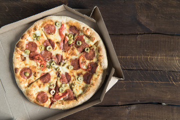 Top view of delicious fresh pizza in cardboard box on wooden table