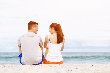 Young couple looking at each other while sitting on beach