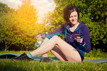 Young athletic woman has a rest after the sports training in the city park. The girl listens to music during workout