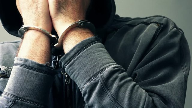 Arrested computer hacker and cyber criminal with handcuffs wearing hooded jacket hiding face