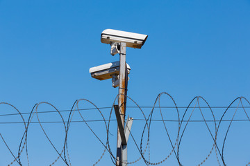 Barbed wire fence with security camera on blue sky