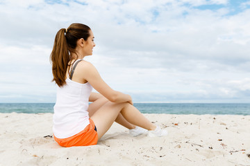 Fototapeta na wymiar Young woman in sports wear sitting at the beach