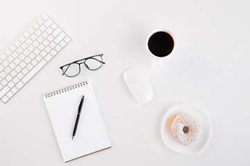 Top view of blank notebook with pen, eyeglasses, keyboard, computer mouse, cup of coffee and tasty doughnut at workplace