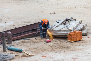 Welder working at construction site. Worker in helmet welds a metal bar