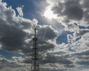 Smoking chimney of oil refinery against cloudy sky and sun