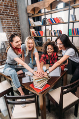 Cheerful young women stacking hands on pile of books