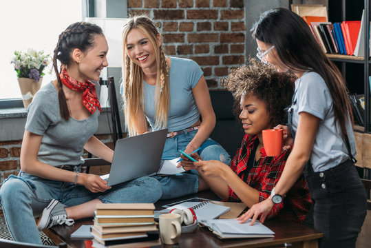 Beautiful smiling young classmates studying together with books and digital devices