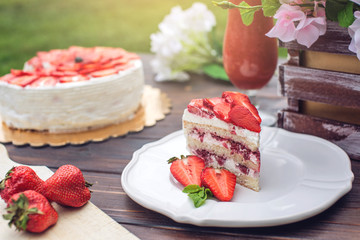 Delicious homemade summer cake with strawberries and butter cream on a wooden porch and a piece on the plate
