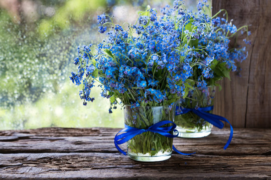 Fototapeta flowers forget-me-nots in glasses tied a blue ribbon on a wooden sill against the window and rain