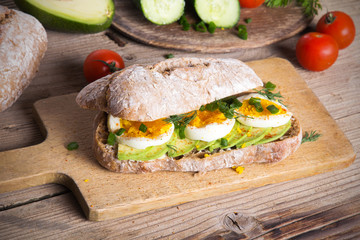 Avocado and egg sandwich on a wooden background. Fresh organic vegetables, eggs and whole wheat bread. Healthy breakfast. Rustic style.