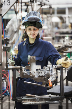Female skilled factory worker holding welding tool, working on cycle frames