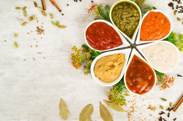 An assortment of sauces in a form of flower with spices on a light gray stone background.
