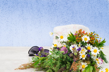A wicker hat, sunglasses and a bouquet of summer field flowers on a white background.