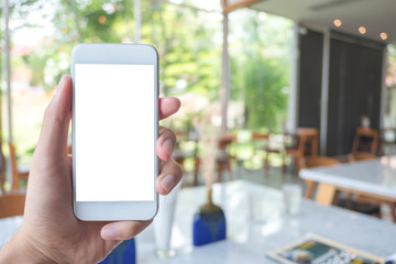 Mockup image of hand holding white mobile phone with blank screen in modern cafe