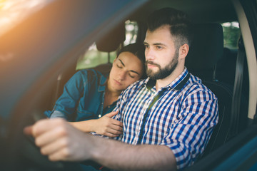 Careful driving. Beautiful young couple sitting on the front passenger seats and smiling while handsome man driving a car