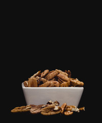White ceramic bowl containing pecan nuts on solid black background