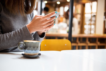 Female hands holding using smartphone with cups of coffee  blurred background made