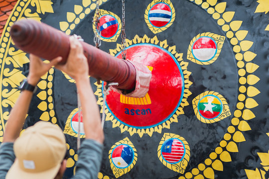 ASEAN gong in Bangkok. Young man holds the beater ready to beat the gong decorated with images of ASEAN flag as well ASEAN countries flags.