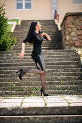 Portrait of young pretty white girl with black hair and in black clothes posing on the old stone staircase.