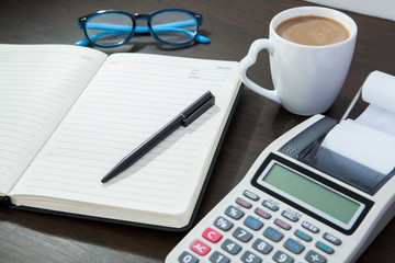 Coffee, notepad with pen and calculator glasses on work table.