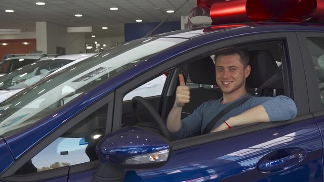 Young male customer showing his thumb up from inside the car at the dealership. Handsome caucasian guy sticking his hand out the window of the vehicle. Attractive brunette man approving purple