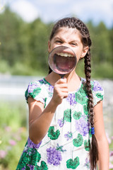 Girl holds magnifying glass and showing opened mouth with teeth