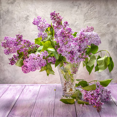 bright lilac bouquet in a transparent glass vase on a wooden table