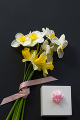 Lovely bouquet of white and yellow narcissus with a pink ribbon and gift box with pink bow on a black background