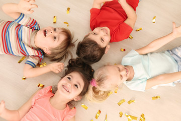 Cute little children with confetti lying on floor at home