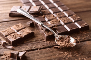 Spoon with cocoa powder and broken chocolate pieces on wooden background
