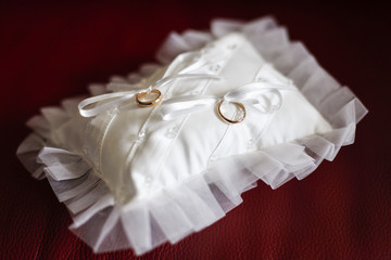 Anelli d'oro legati sopra cuscinetto bianco e sopra tavolo rosso © alex.pin