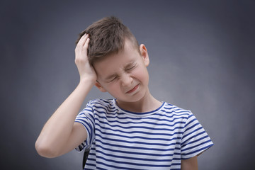 Cute boy suffering from headache on color background