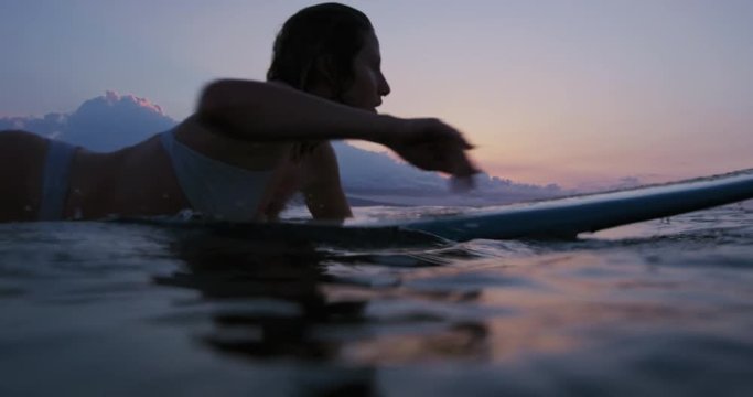 Beautiful young woman surfing in bikini at sunset in slow motion